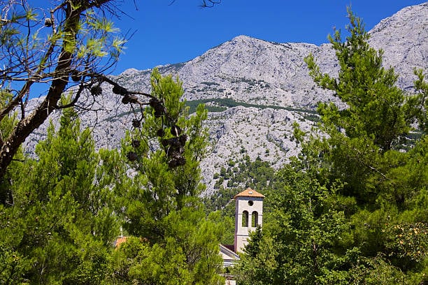 Rocky Biokovo slopes above pine trees and a stone bell tower